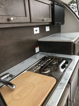 Spacious RV rental kitchen with marble-look counters, stove, sink, dark wood cabinets, and TV. Ready for travel.
