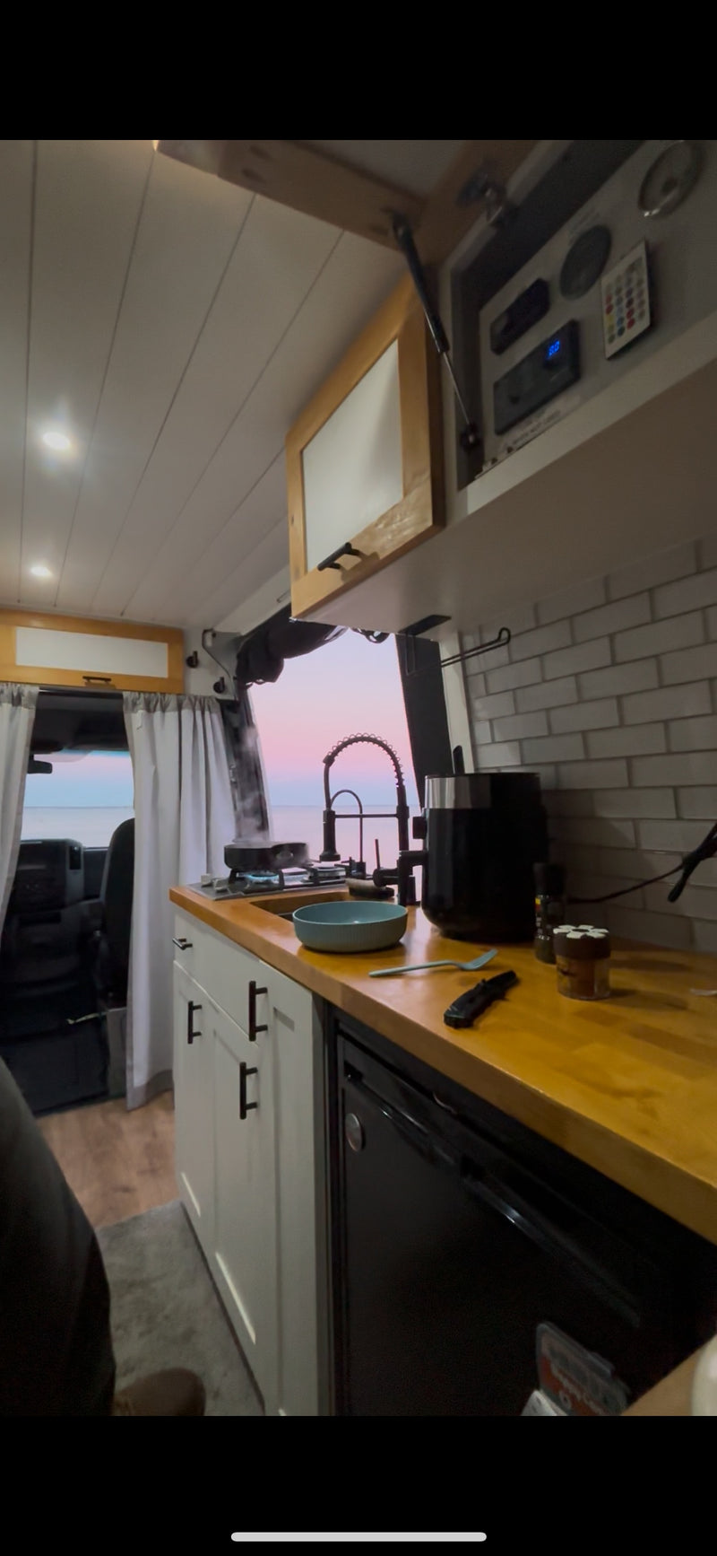 RV rental kitchen with stove and sink, overlooking a beautiful ocean sunset. Cooking dinner in a cozy camper van. — photo 8