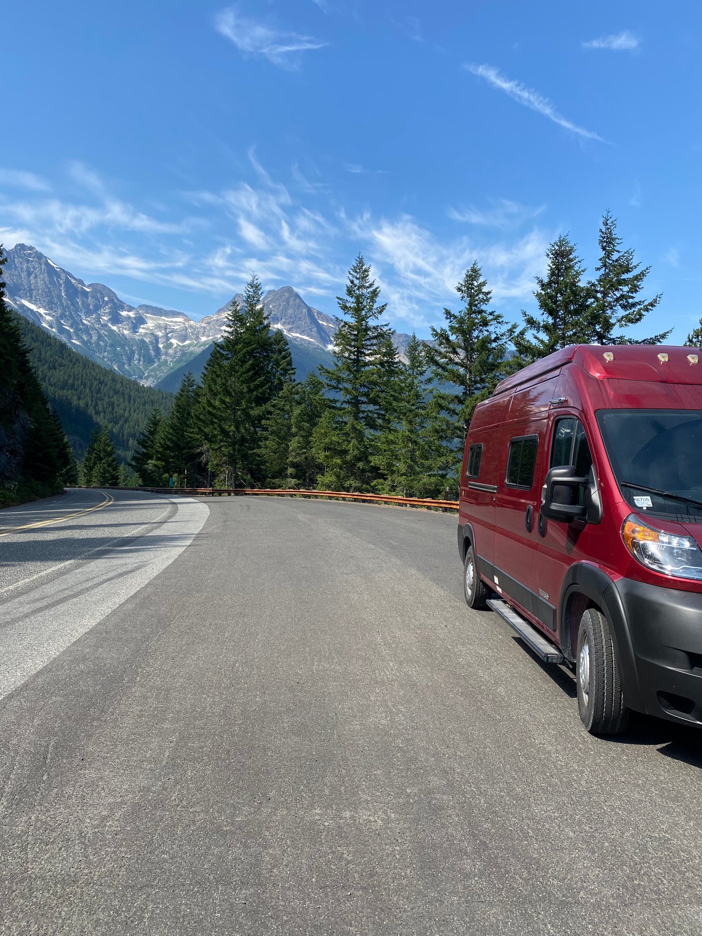 This scenic mountain road trip features a red rv rental, majestic snow-capped peaks, and lush forests under a clear sky.