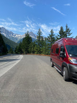 This scenic mountain road trip features a red rv rental, majestic snow-capped peaks, and lush forests under a clear sky.