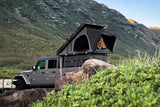 Adventure-ready RV rental! Jeep Gladiator with a rooftop tent parked on rocks near lush mountains for unique outdoor stays.