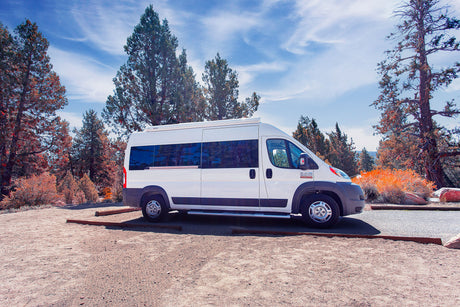White Ram ProMaster camper van parked outdoors amidst trees & blue sky. Ideal for your next RV rental road trip.