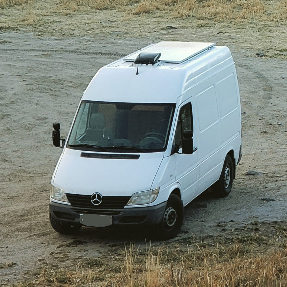 White Mercedes-Benz Sprinter camper van with solar panels & roof vent parked on dirt. Explore this RV rental!