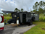 Compact Core RV rental set up at a scenic campsite with awning extended, generator running, and propane hooked up.