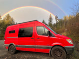 Red RV rental van parked outdoors, beneath a stunning double rainbow. Ready for adventure!