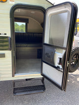 View of an RV rental's open door, revealing its interior bench, screen door, and pull-out step. Ready for your trip!
