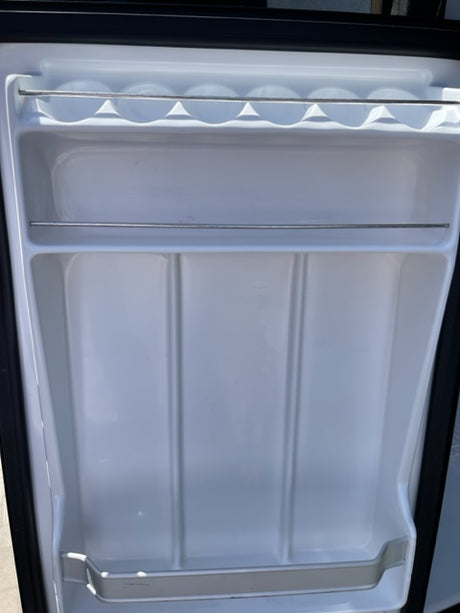 Empty, clean mini-fridge interior in an RV rental. Features a beverage caddy & molded shelf slots for organized storage.