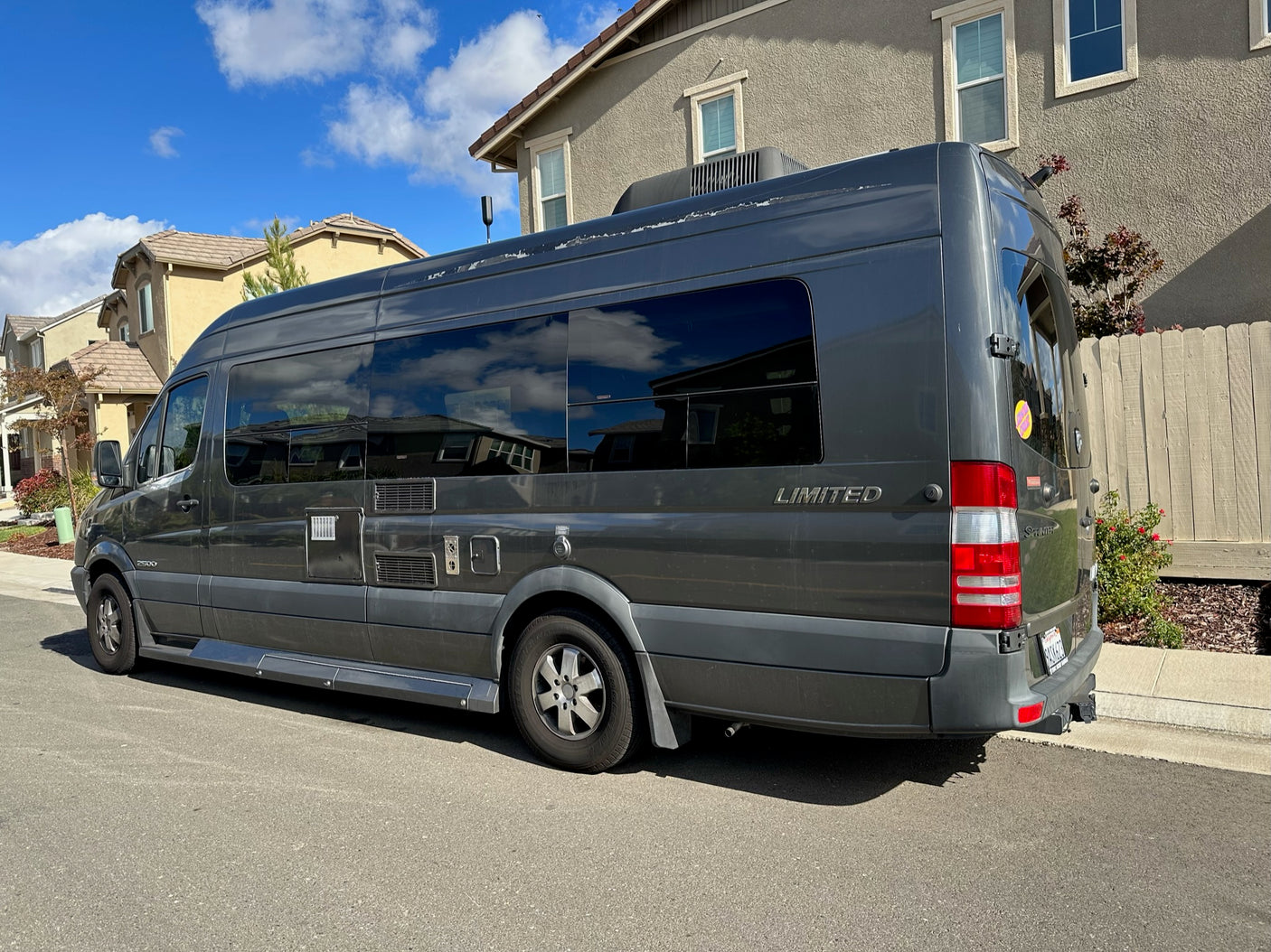 This dark gray Mercedes Sprinter 2500 camper van, often used as an RV rental, is parked on a residential street.