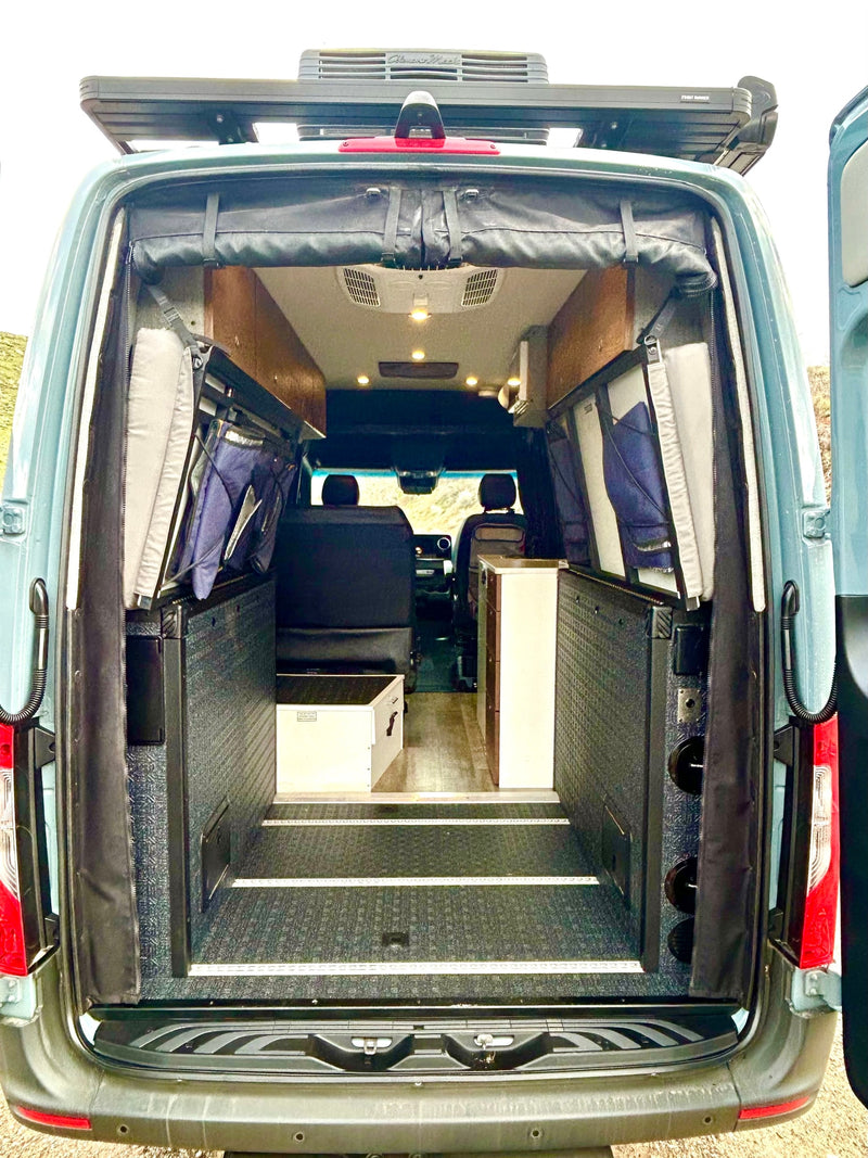 Experience a custom RV rental! Rear view of a spacious camper van interior with folded beds & storage, perfect for mobile travel. — photo 13