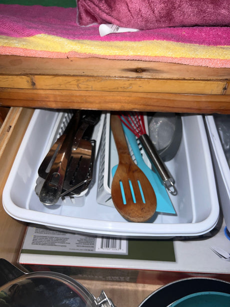 Essential kitchen utensils in an organized drawer in an RV rental, with colorful towels on the shelf above.