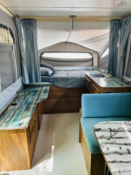 Cozy pop-up RV rental interior with bed, custom counters (sink, dining), and blue accents. Ready for your trip!