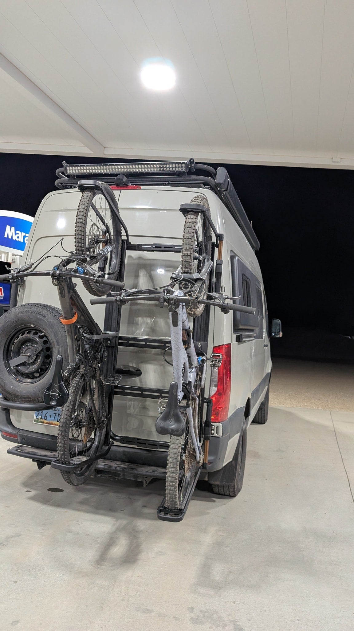 RV rental van with two mountain bikes on a rear rack & spare tire, parked at a gas station canopy at night, ready for adventure. — photo 5