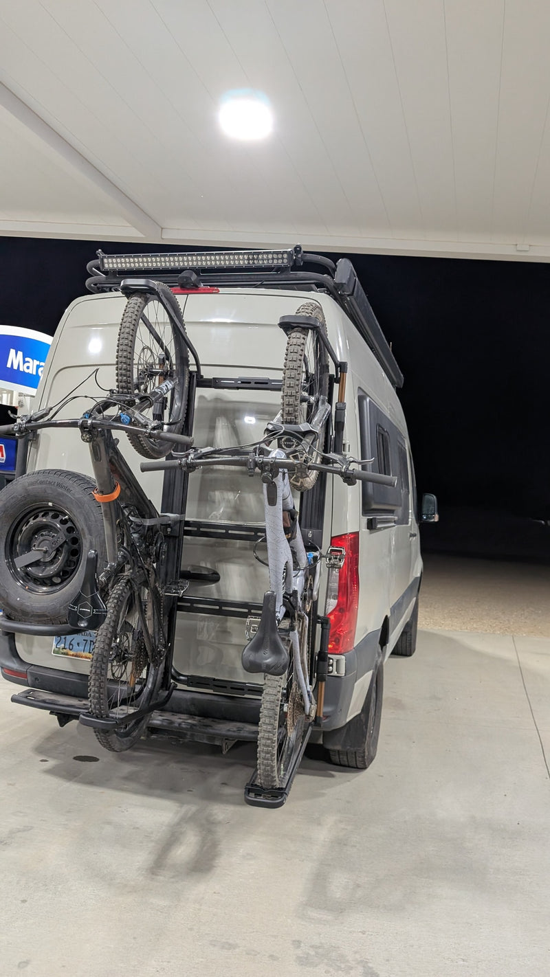 RV rental van with two mountain bikes on a rear rack & spare tire, parked at a gas station canopy at night, ready for adventure. — photo 5