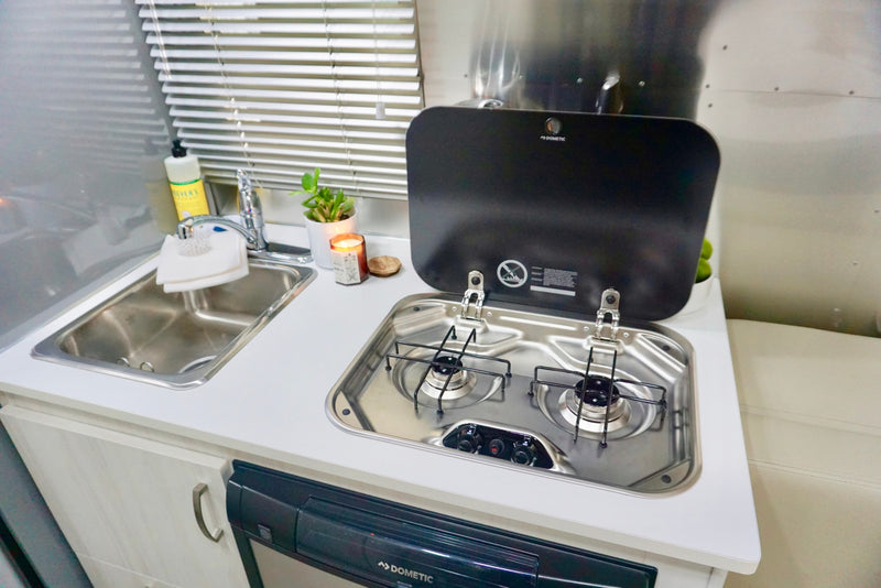 Bright RV rental kitchen with stainless steel sink, two-burner Dometic stove, white counters, and small decor. — photo 15