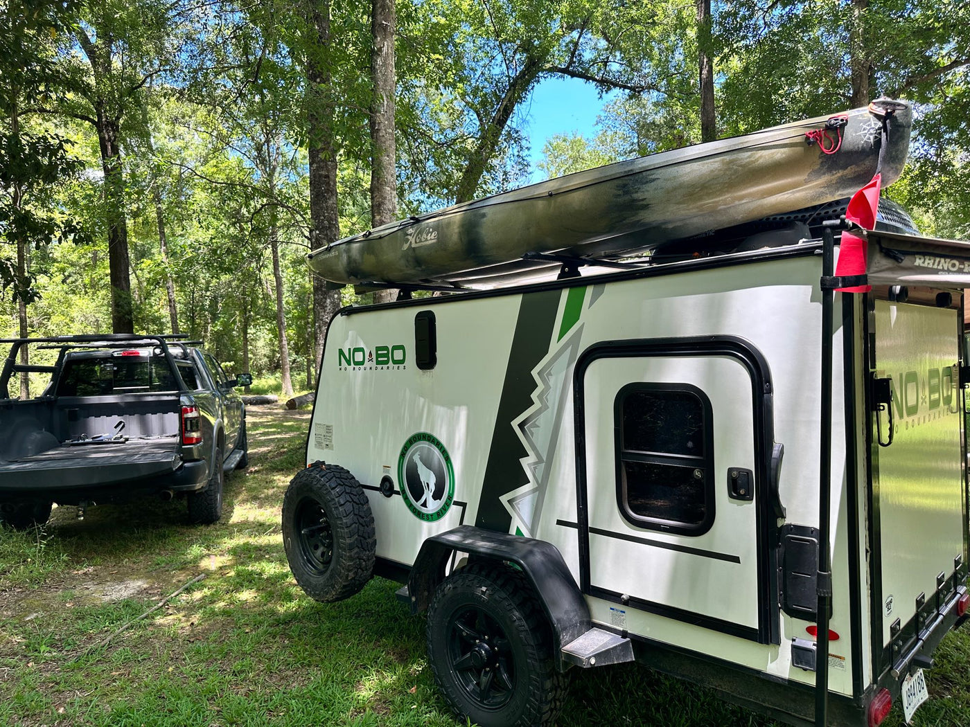 An RV rental camper with a kayak atop, parked with a truck in a wooded campsite, ready for adventure. — photo 15