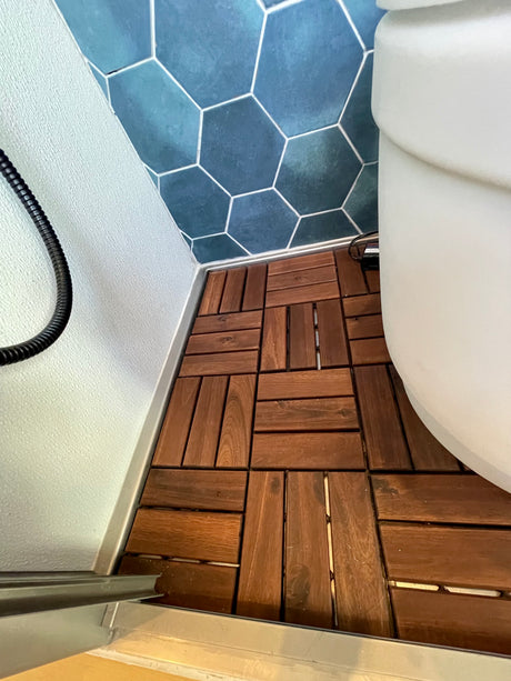 Compact bathroom design in an RV rental, featuring blue hexagonal wall tiles and brown wood-look interlocking floor tiles.