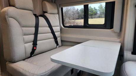 Comfortable RV rental interior with bench seating, two seatbelts, a folding table, and scenic window view.