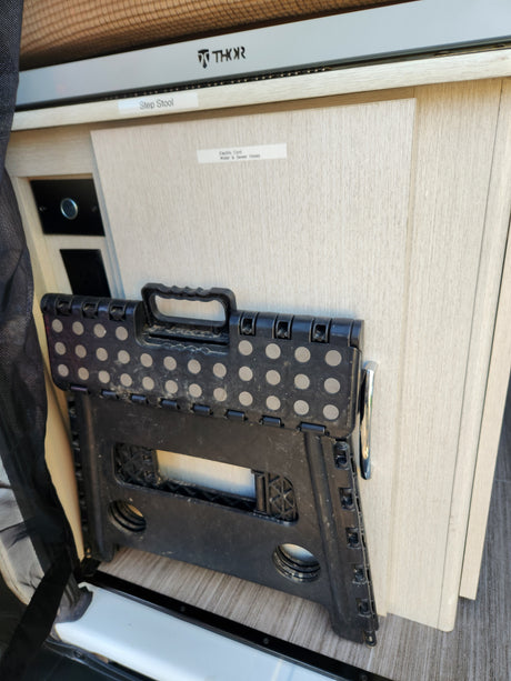 THOR RV rental interior: a black foldable step stool and labels for cords, hoses, and step stool storage.