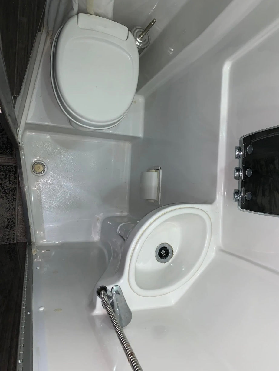 Compact RV rental wet bath featuring a white toilet, small sink with shower faucet, and toilet paper holder. All-in-one convenience.