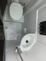 Compact RV rental wet bath featuring a white toilet, small sink with shower faucet, and toilet paper holder. All-in-one convenience.