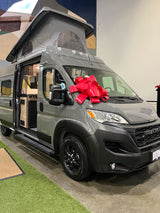 Grey Winnebago Ram camper van, featuring a pop-top and red bow, showcased for potential RV rental. Interior is visible.