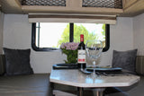 Relax in this RV rental's inviting dinette, featuring wine, fresh flowers, and comfortable seating with pillows.