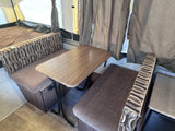 RV rental: Pop-up camper interior with wood-look dinette table, patterned seating, and bed area.