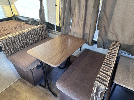 RV rental: Pop-up camper interior with wood-look dinette table, patterned seating, and bed area.