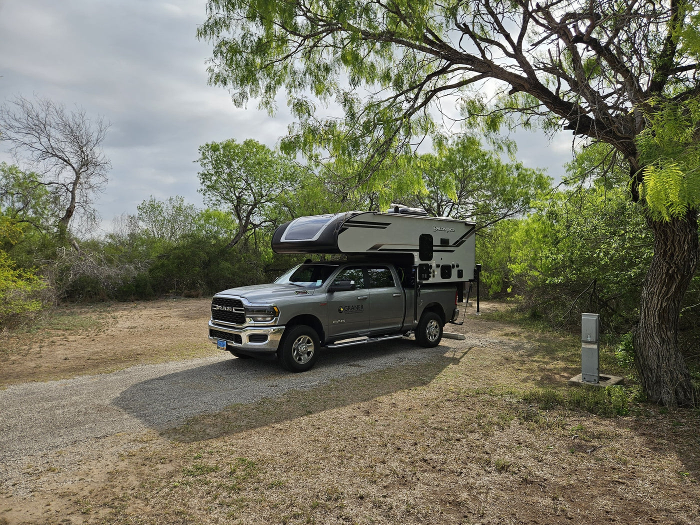 An RV rental truck camper (Palomino) on a grey RAM truck, parked at a rustic campsite with utilities. — photo 11