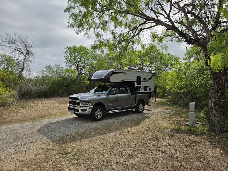 An RV rental truck camper (Palomino) on a grey RAM truck, parked at a rustic campsite with utilities. — photo 11