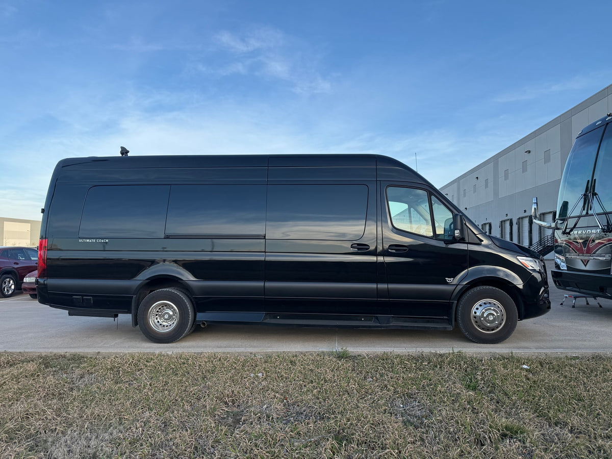 Black luxury coach van, ideal for RV rental, with "ULTIMATE COACH" branding visible on its side, parked outdoors.