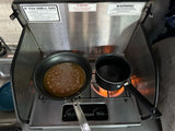 Cooking a pancake and boiling water on an RV rental stove, complete with safety warnings in a compact kitchen.