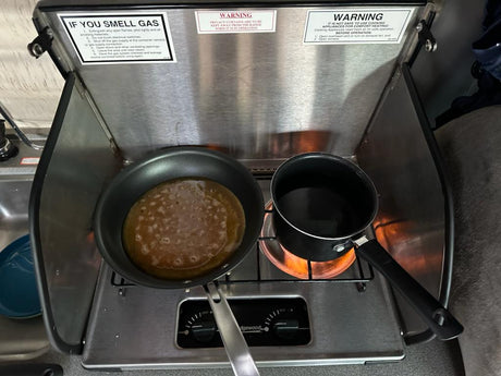 Cooking a pancake and boiling water on an RV rental stove, complete with safety warnings in a compact kitchen.