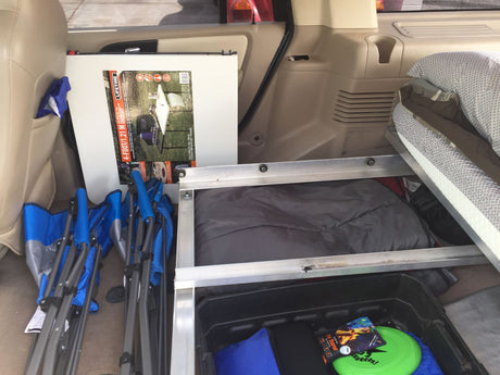 RV rental packed for camping: folding table, chairs, sleeping bag, and a bin of essentials in the cargo area.