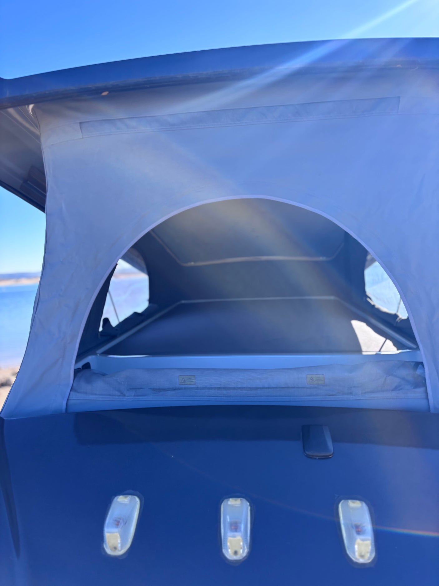 A blue pop-top camper, extended and open, overlooking water. An ideal rv rental for outdoor adventures.