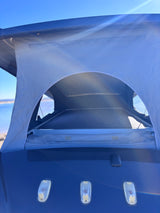 A blue pop-top camper, extended and open, overlooking water. An ideal rv rental for outdoor adventures.