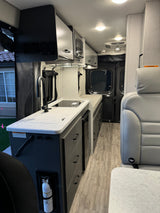 Explore this modern RV rental interior featuring a compact kitchen, sink, stove, microwave, and cozy living space.