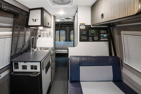 Bright rv rental interior with kitchen sink, fridge, control panel, and rear bed. Modern camper van layout.