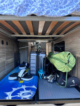 Under-bed storage in an rv rental, showcasing a wakeboard, Delsey suitcase, golf clubs, and other adventure gear.