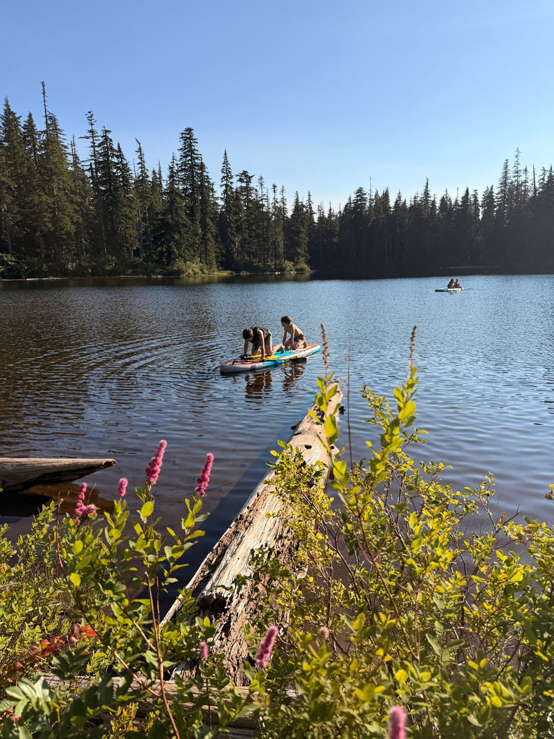 A tranquil forest lake with kids paddleboarding. A fallen log and pink flowers frame the view. Ideal for an RV rental vacation. — photo 17