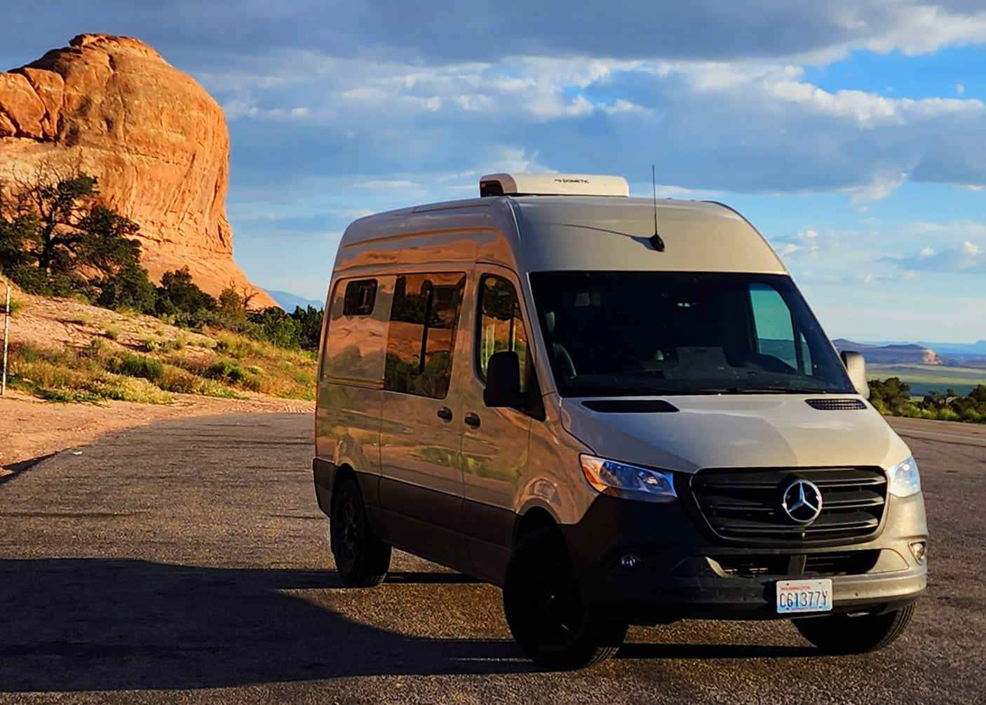 Scenic desert view with a Mercedes Sprinter van RV rental parked on a road beside a massive rock formation.