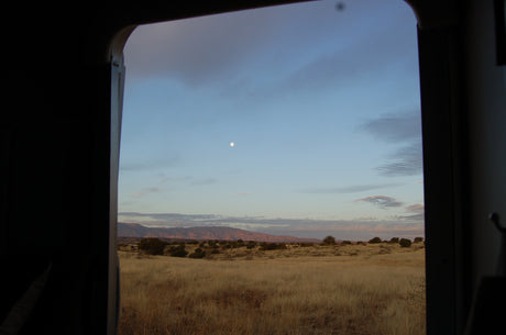Scenic RV rental view: Moonlit desert landscape from a travel vehicle window at dusk.