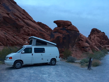 Experience nature! This white pop-top RV rental is perfectly parked on a dirt road by magnificent red rock mountains.