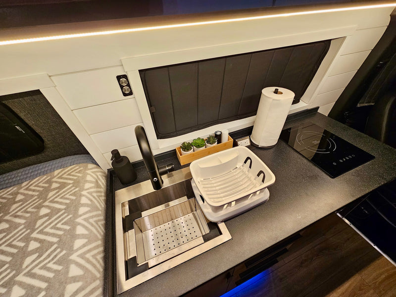 Modern RV rental kitchen with a black faucet, induction cooktop, and handy dish drying rack for compact living. — photo 18