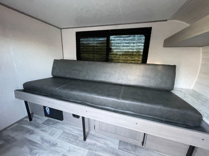 An RV rental's versatile interior features a grey sofa bed, window, and storage. Ideal for travel comfort.