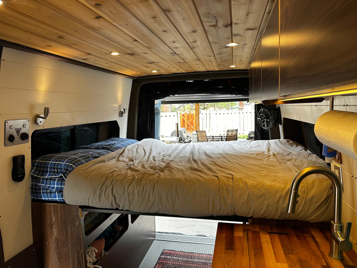 Cozy RV rental interior: bed, wooden ceiling, compact kitchenette, and view of outdoors from open back. — photo 14