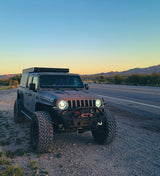 Gray modified Jeep Gladiator truck with a rooftop camper, parked on a desert road at dusk. A unique RV rental for off-road adventure.