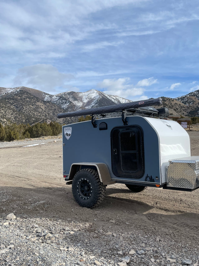 Rugged teardrop camper, ideal for an RV rental mountain adventure. Ready for off-grid exploration in the snow-capped terrain.