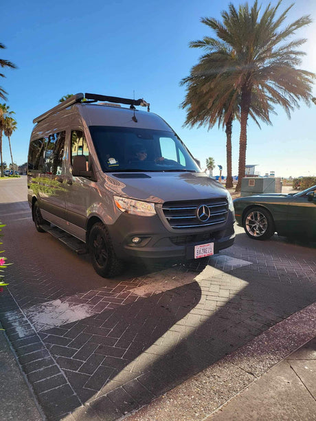Explore the coast! This sleek gray Mercedes Sprinter RV rental is ready for adventure under sunny skies near the beach.