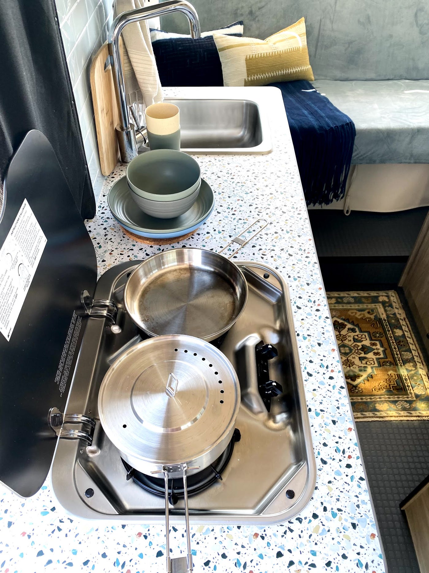 RV rental kitchen features a speckled countertop, sink, and two-burner stovetop with pans and pots, ideal for travel. — photo 6